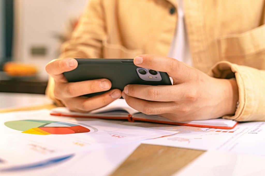 pexels-photo-8374258-8374258 A business person checking their phone while working with graphs and charts on a desk.
